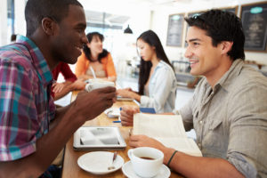 Two Male Friends Meeting In Busy Coffee Shop