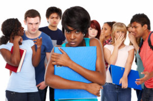 Teenage girl looks apprehensively at the camera while her classmates gossip behind her back. Horizontal shot. Isolated on white.