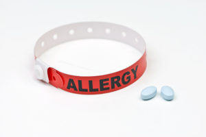 Allergy alert hospital wristband with blue medication tablets.